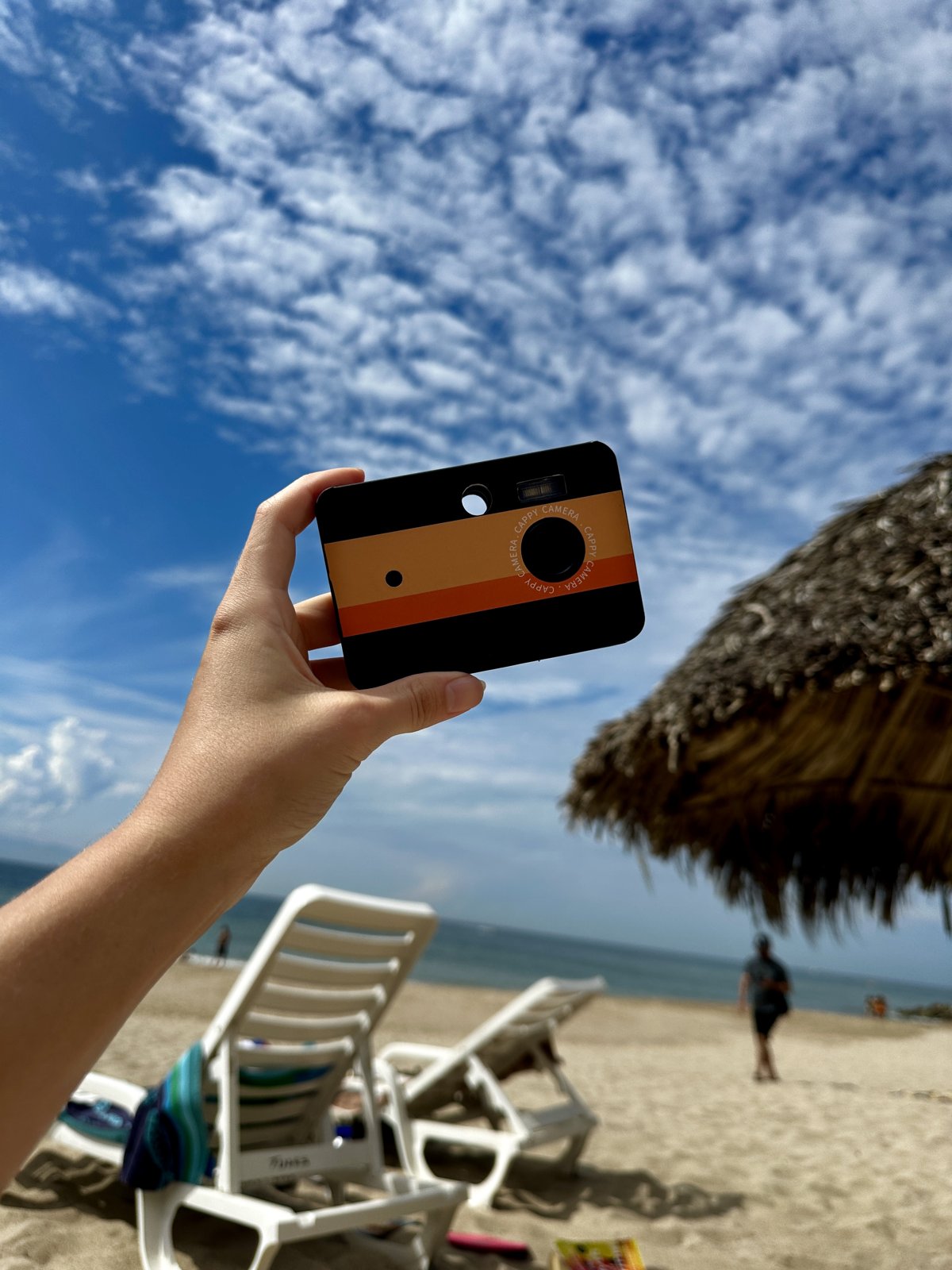 Hand holding a Cappy Camera up to a blue beach sky
