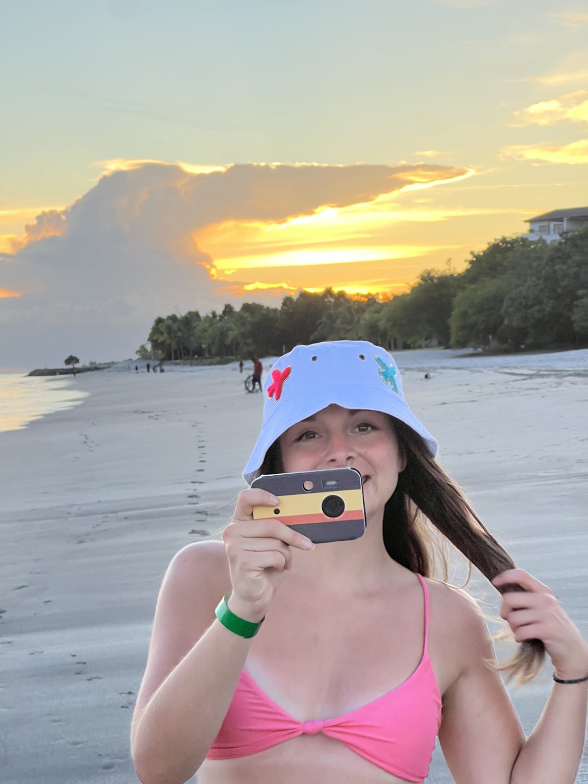 Girl in a bucket hat holding a Cappy Camera on the beach at sunset